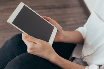 Mockup image of a woman sitting and holding white tablet pc with blank desktop screen