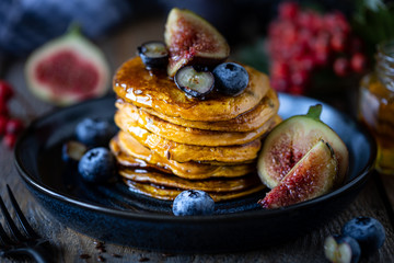 Pumpkin pancakes with syrup or honey, flax seeds, figs, blueberries in a dark plate on the table,...