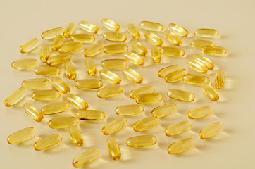 Yellow transparent oval capsules with fish oil. Light glass surface. A scattering of tablets. The concept of fertility in the pharmaceutical industry. Close-up