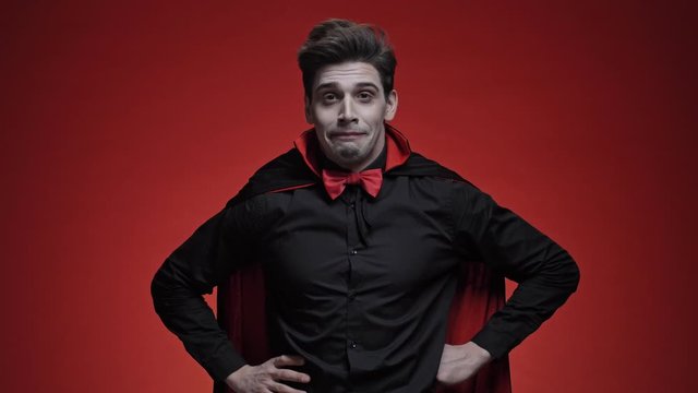 Vampire man in black halloween costume is sneezing and losing his fangs isolated over red wall