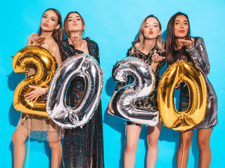 Fototapeta na wymiar Beautiful Women Celebrating New Year. Happy Gorgeous Girls In Stylish Sexy Party Dresses Holding Gold and Silver 2020 Balloons,Having Fun At New Year's Eve Party.Holiday Celebration.They give air kiss