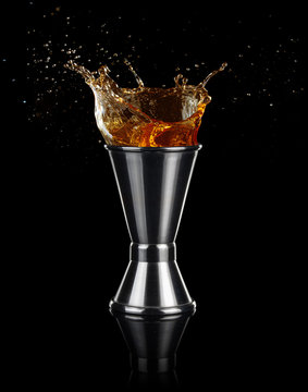 liquor splashing out of a jigger isolated on black background