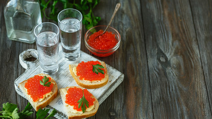 Vodka with salmon caviar and bread toast on wooden background. Alcohol pure craft drink and traditional snacks. Negative space. Celebrating food and delicious. Top view.