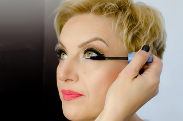 Obraz premium make-up artist applying black mascara on eyes with brush. Beautiful woman eyes make-up. Senior blonde woman with fresh healthy skin and perfect professional makeup 