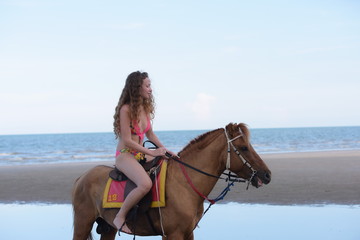 Beautiful girl in a swimsuit is happily riding a horse on the sand.