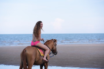 A pretty woman in a bikini is happily riding a horse on the beach.