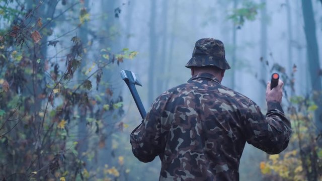 Rear view of Brutal man with an ax and a flashlight walks through the forest