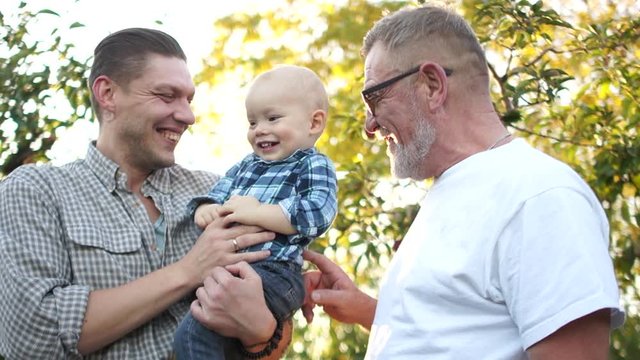Grandfather, son and grandson laugh merrily against the backdrop of the rays of the setting sun. A happy family has fun in the apple orchard. Fathers day
