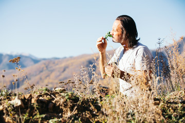 A man on the side of a mountain collects medicinal aromatic herbs.