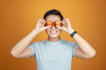 Young Asian man take fun with tomatoes. Isolated on orange background