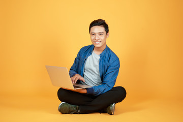 Asian man use of the laptop computer against color orange background