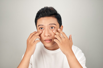 Closeup portrait of smiling adult Asian business man pointing to his eye and touching cheek. Isolated front view on white background.