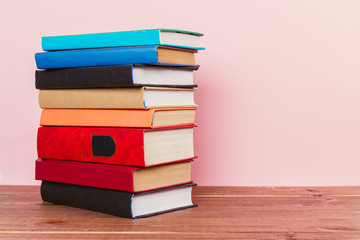 A simple composition of many hardback books, raw books on a wooden table and a pale pink background