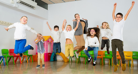 Fototapeta premium Children with teacher jumping together in schoolroom
