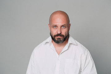 Serious middle-aged man with folded arms and a deadpan expression posing in front of a gray background with copy space