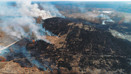 Forest and field fire. Dry grass burns, natural disaster. Aerial view. A large burned field, burning occurs on the banks of a small river.
