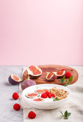 Fototapeta na wymiar Yoghurt with raspberry, granola and figs in white plate on a gray and pink background and linen textile. side view.