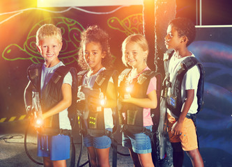 Group portrait of positive smiling teenagers with laser guns having fun on dark lasertag arena