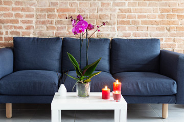 Living room table with orchid flowerpot, candles and air refresher sticks in modern interior design.