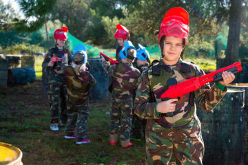Boy paintball player in camouflage standing with gun before playing outdoors