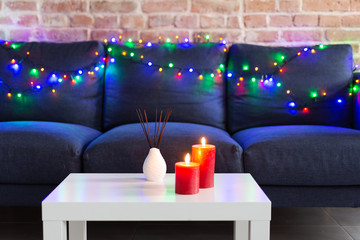 Room air refresher sticks and red burning candles on table on home modern interior.