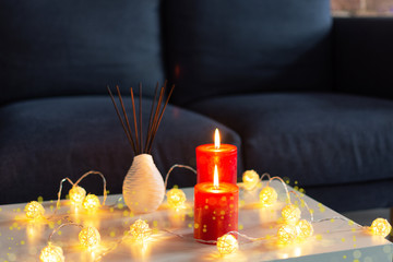 Room air refresher sticks and red burning candles on table on home modern interior.
