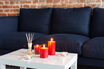 Room air refresher sticks and red burning candles on table on home modern interior.