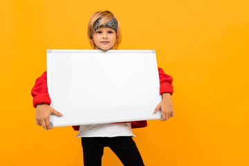 charming boy bully looks at the camera on a yellow background, holds in his hands a white blank poster for text