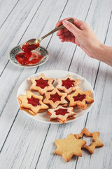 Woman's hand is picking up jam with a vintage spoon to fill some delicious handmade star cookies....