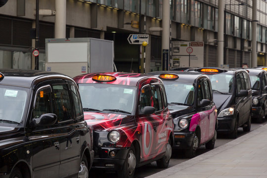 Row of stationary London taxi cabs queuing at a taxi rank waiting for a fare