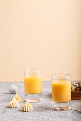 Sweet egg liqueur in glass with quail eggs and meringues on a gray and orange background. Side view