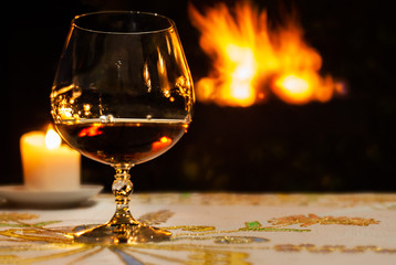 One glass of brandy on a table and big fire on the black background
