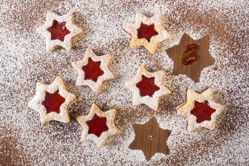 Top view of handmade star cookies stuffed with jam on a rustic wooden table and covered with icing sugar. The cookies are disappearing from the table. Strawberry, raspberry, currant jam cookies
