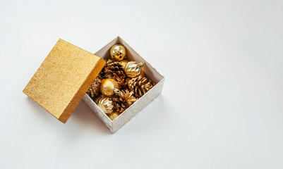 Box with golden christmas decorations on a white background. Golden Christmas balls and fir cones.
