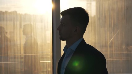 Young wealthy businessman in stylish suit walking through glass hall of modern office build. Profile of successful man going to home after hard working day. Handsome guy stepping indoor. Slow motion