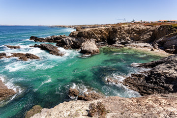 Fototapeta na wymiar Enseada de águas transparentes protegida das ondas do mar pelos rochedos no Alentejo em Portugal.
