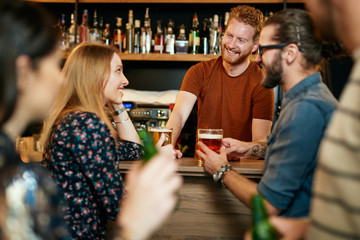 Group of friends drinking beer, chatting and talking to barman. Night out. Pub interior.