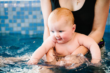 Enjoy the first day of swimming in the water. Mom holds child preparing for diving. doing exercises. Young mother, swimming instructor and happy little girl in the pool. Teaches infant child to swim