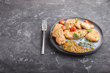 Fried pork chops with tomatoes and herbs on a gray ceramic plate on a black concrete background. side view.