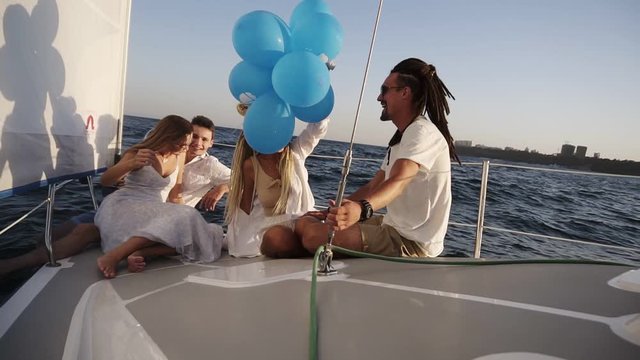 Four friends having relaxing cruise on the yacht while lying on a bow of the boat. They enjoying the moment - girl in a white waving the balloones, celebating. Slow motion. Sunny day spending outdoors