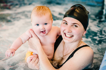 whirlpool, jacuzzi. Diving baby in the paddling pool. Young mother, swimming instructor and happy little girl in pool. Learn infant child to swim. Enjoy the first day of swimming in water.