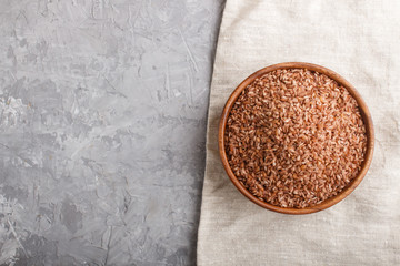 Wooden bowl with unpolished brown rice on a gray concrete background. Top view, copy space.