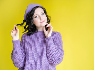 Beautiful young girl in a lilac hat and in a lilac sweater on a yellow background close-up