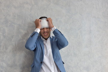 Overworked businessman with bandaged hurt head at workplace with scattered documents