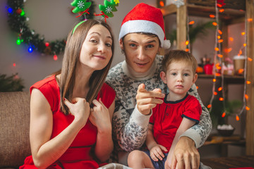 Mom and dad give their son a gift in a red box. A young family with a child celebrates Christmas and New year at home