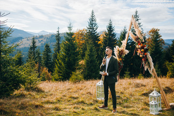Amazing man in green suit stands near arch on mountains background