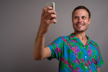 Portrait of handsome tourist man using phone ready for vacation against gray background