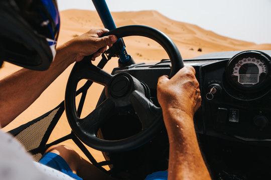 Man hands driving a buggy in the desert dunes. View from the cockpit.