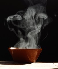bowl of hot soup with steaming on wooden table on black background