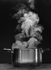 Steaming pot on black background. Smoke above boiling soup pot. 